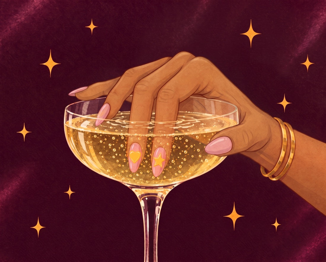 Mano mojando dos uñas con pegatinas de corazón y estrella en una copa de cava, con la otra mano apoyada en el borde